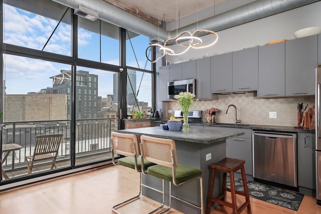 kitchen with stainless steel appliances, a sink, dark countertops, gray cabinetry, and expansive windows
