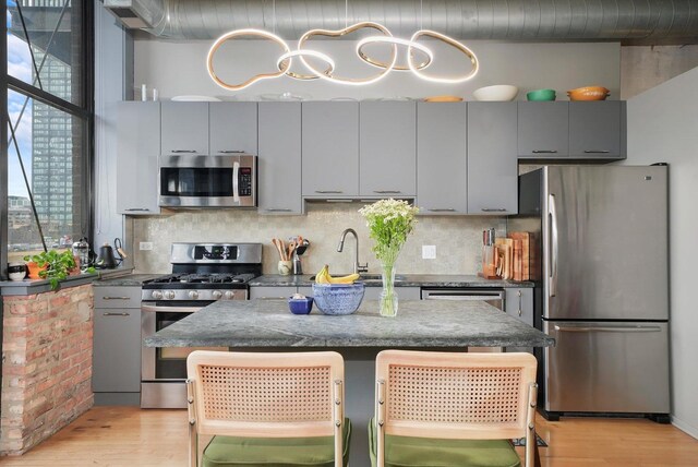 kitchen featuring appliances with stainless steel finishes, gray cabinetry, a sink, light wood-type flooring, and backsplash