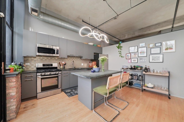 kitchen featuring appliances with stainless steel finishes, gray cabinetry, dark countertops, and light wood finished floors