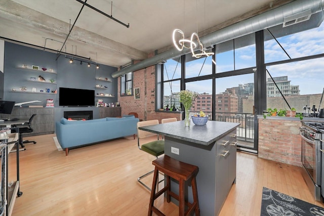 kitchen featuring light wood-type flooring, stainless steel gas range oven, a kitchen island, a chandelier, and a kitchen bar