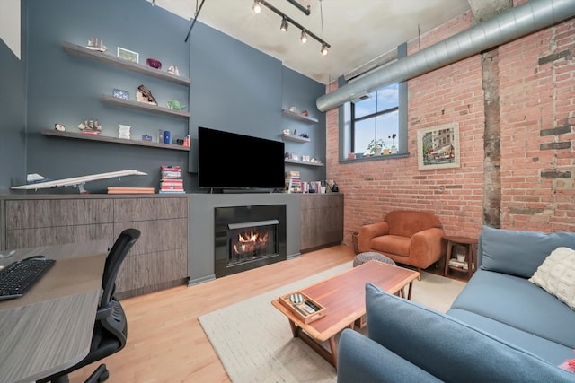 living area featuring wood finished floors, brick wall, and a glass covered fireplace