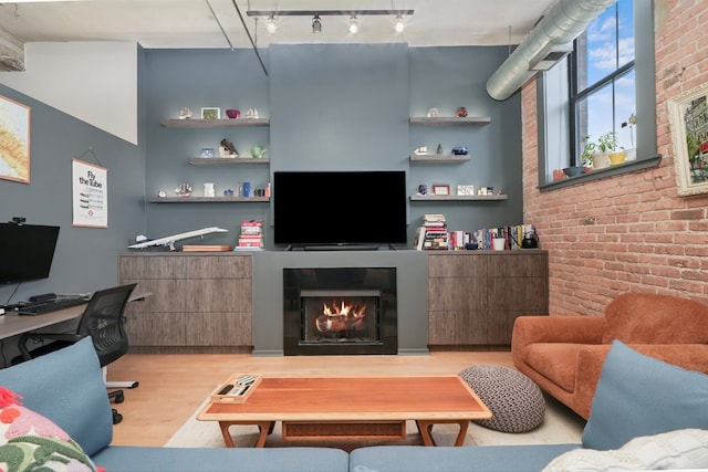 living room with light wood finished floors, a lit fireplace, brick wall, track lighting, and an office area