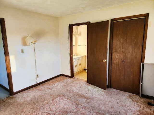 unfurnished bedroom with light colored carpet, baseboards, connected bathroom, a sink, and a closet