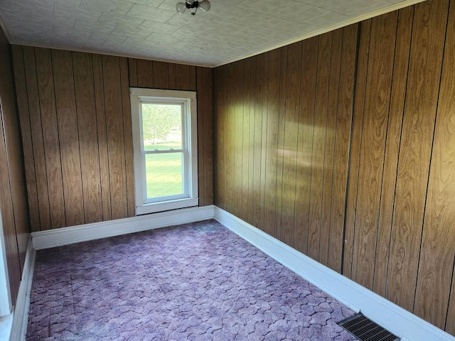 carpeted spare room featuring wood walls and baseboards