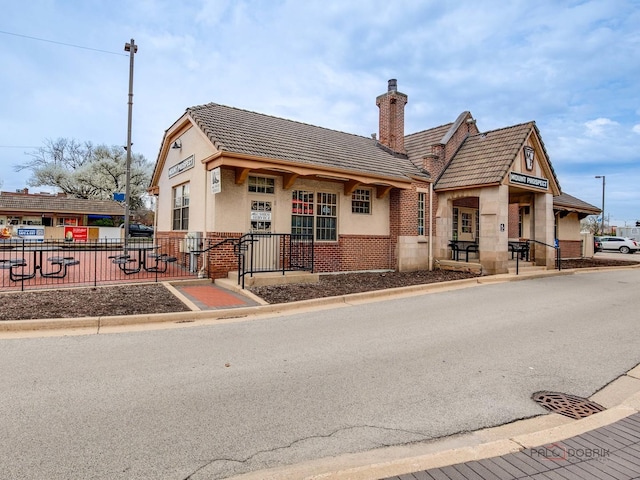 5 W Central Rd Unit 512, Mount Prospect, IL 60056 - view of front facade featuring fence, brick siding, a chimney, a tiled roof, and stucco siding
