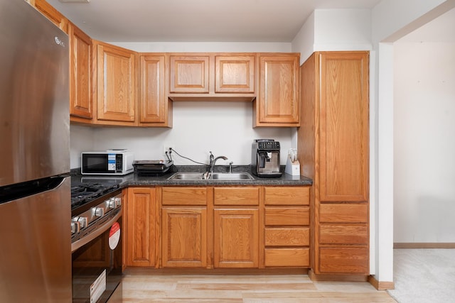 kitchen featuring stainless steel appliances, a sink, dark countertops, and light wood-style flooring