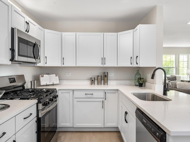 kitchen featuring appliances with stainless steel finishes, a sink, white cabinets, light wood-style flooring, and a peninsula