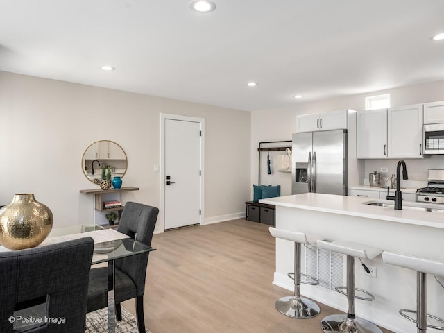 kitchen with appliances with stainless steel finishes, a sink, light countertops, light wood-style floors, and baseboards