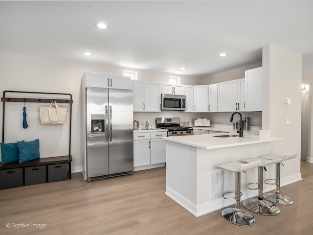 kitchen featuring stainless steel appliances, a sink, light countertops, a peninsula, and light wood-style floors