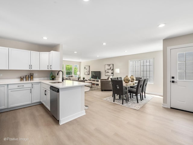 kitchen featuring dishwasher, a sink, light wood finished floors, a peninsula, and light countertops