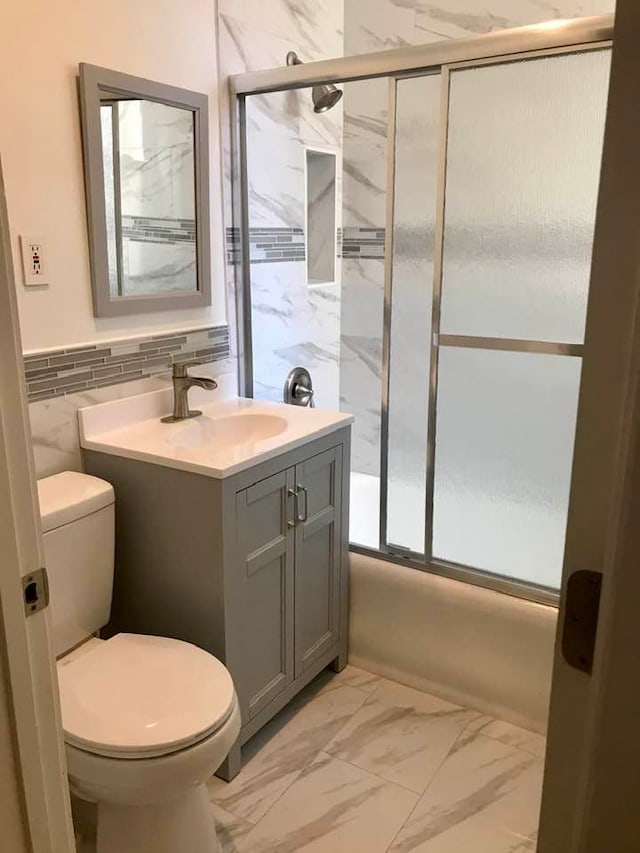 bathroom with marble finish flooring, shower / bath combination with glass door, toilet, tile walls, and vanity