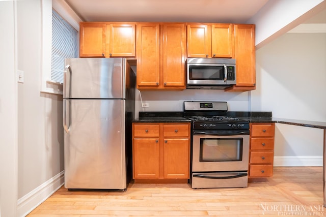 kitchen featuring appliances with stainless steel finishes, light wood finished floors, dark stone counters, and baseboards