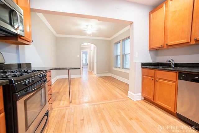 kitchen featuring stainless steel appliances, light wood-style floors, ornamental molding, arched walkways, and a sink