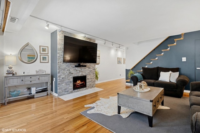 living room featuring track lighting, wood finished floors, and a stone fireplace