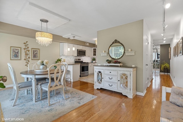 dining room with light wood finished floors, rail lighting, baseboards, and a chandelier