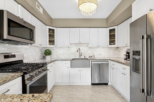 kitchen featuring appliances with stainless steel finishes, a sink, light marble finish flooring, a chandelier, and light stone countertops