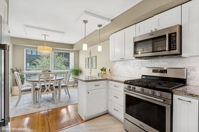 kitchen with stainless steel appliances, white cabinets, a peninsula, light stone countertops, and decorative backsplash