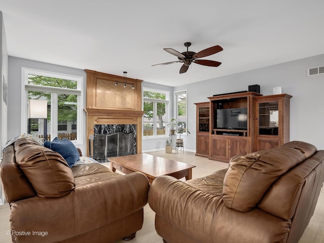 living area with a ceiling fan, a fireplace, plenty of natural light, and light wood finished floors