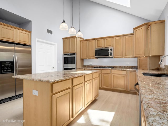 kitchen featuring stainless steel appliances, a sink, high vaulted ceiling, light wood-style floors, and a skylight