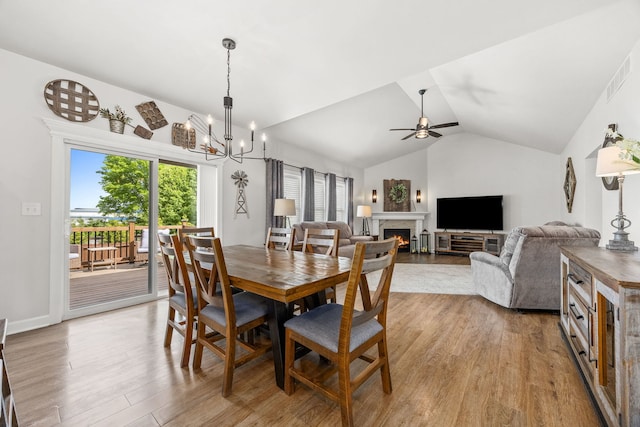 dining room with light wood-style floors, a lit fireplace, lofted ceiling, ceiling fan, and a chandelier