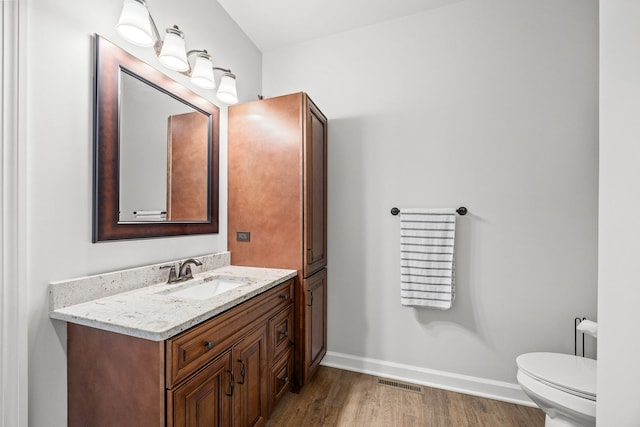 half bath featuring wood finished floors, vanity, baseboards, and toilet