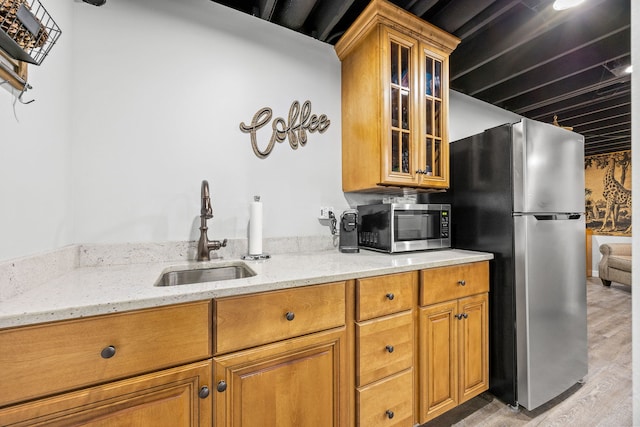 kitchen featuring a sink, stainless steel appliances, light stone countertops, light wood-type flooring, and glass insert cabinets