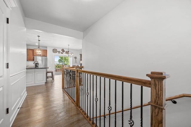 hall with light wood-type flooring, an upstairs landing, a chandelier, and a sink