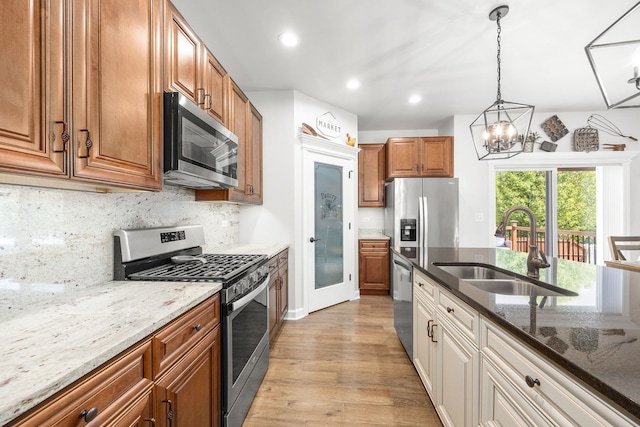 kitchen with stainless steel appliances, a sink, light wood-style floors, a chandelier, and dark stone counters