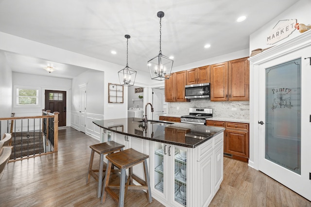 kitchen featuring a sink, stainless steel appliances, a chandelier, light wood-style floors, and a center island with sink