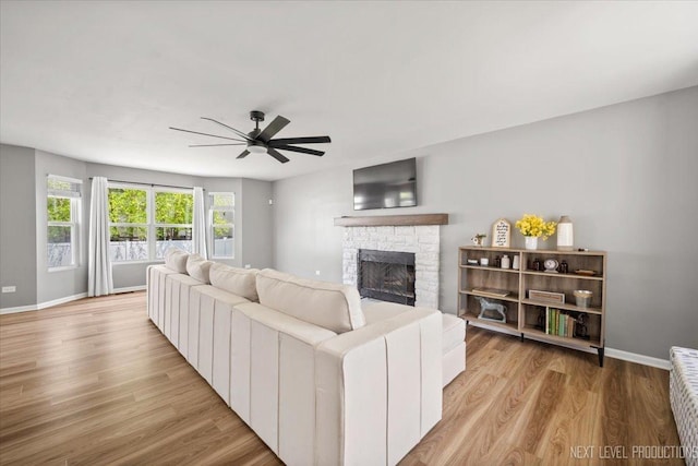 living area with a ceiling fan, a fireplace, light wood-style floors, and baseboards