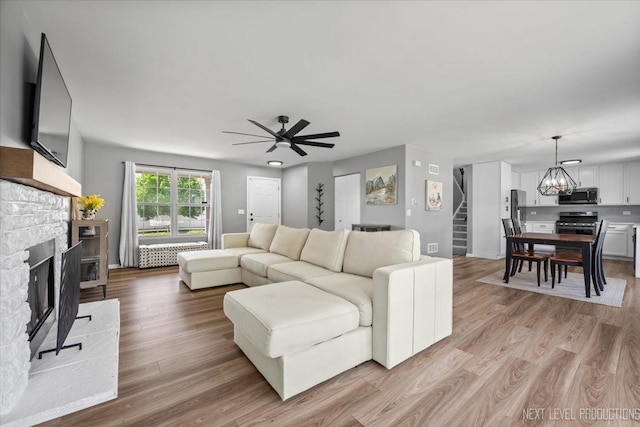 living room featuring stairs, a fireplace, a chandelier, and light wood-type flooring