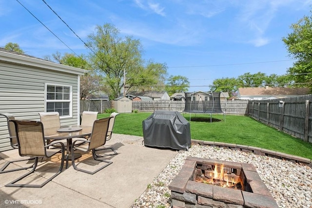 view of patio / terrace with a shed, an outdoor fire pit, outdoor dining space, an outbuilding, and a trampoline
