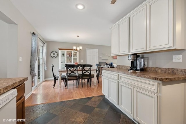kitchen with white dishwasher, white cabinetry, a chandelier, dark stone finish floors, and hanging light fixtures