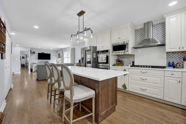 884 Arnold Ct, Des Plaines, IL 60016 - kitchen featuring wall chimney range hood, appliances with stainless steel finishes, a kitchen island, tasteful backsplash, and light wood finished floors