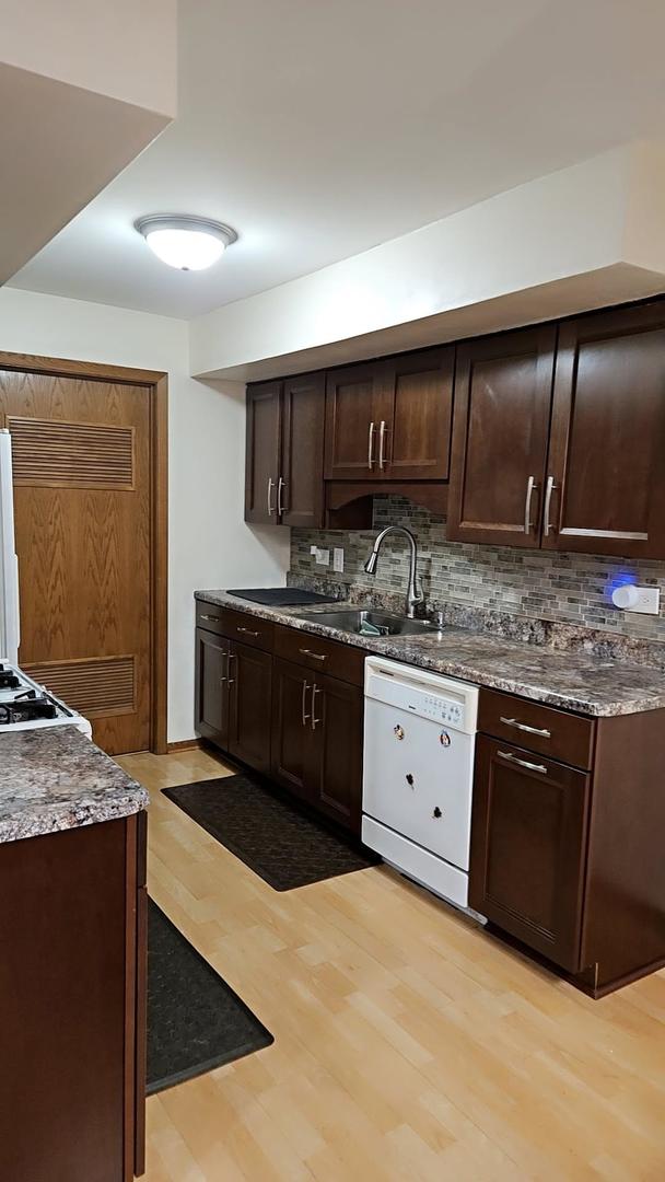 9230 Hartwood Ct Unit 1404, Orland Park, IL 60462 - kitchen with white dishwasher, a sink, tasteful backsplash, dark brown cabinets, and light wood-type flooring