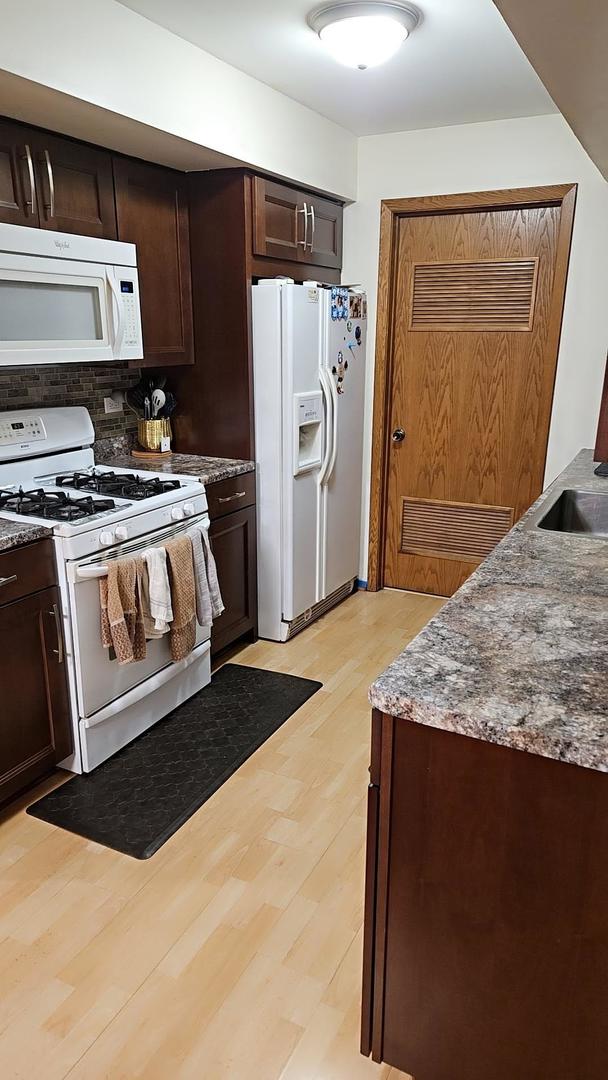 9230 Hartwood Ct Unit 1404, Orland Park, IL 60462 - kitchen with white appliances, dark brown cabinetry, light wood finished floors, tasteful backsplash, and stone countertops