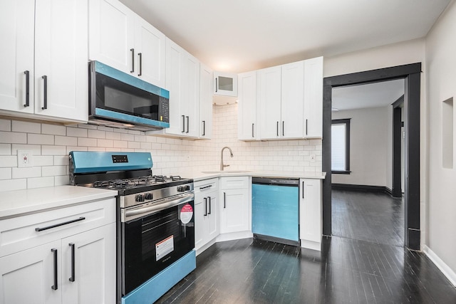 kitchen with appliances with stainless steel finishes, light countertops, a sink, dark wood finished floors, and backsplash