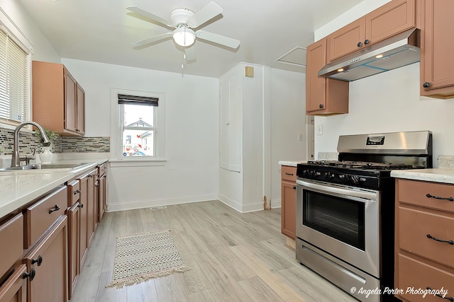 kitchen featuring stainless steel gas range, under cabinet range hood, a sink, light countertops, and ceiling fan