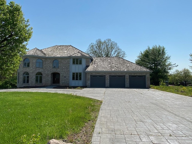 french country style house featuring decorative driveway, an attached garage, and a front lawn
