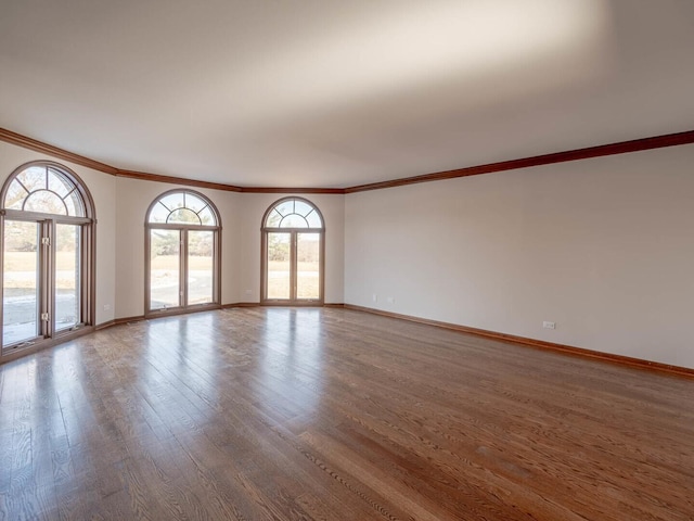 spare room with wood finished floors, ornamental molding, plenty of natural light, and baseboards