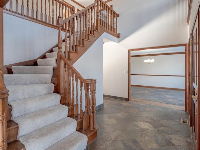 stairway with baseboards, a chandelier, a towering ceiling, and stone finish floors