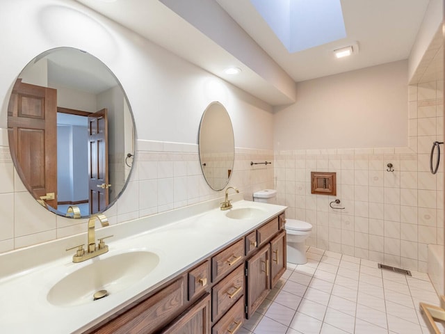 bathroom featuring toilet, tile walls, double vanity, wainscoting, and tile patterned floors