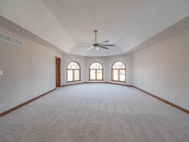 carpeted empty room with a ceiling fan, a raised ceiling, and baseboards