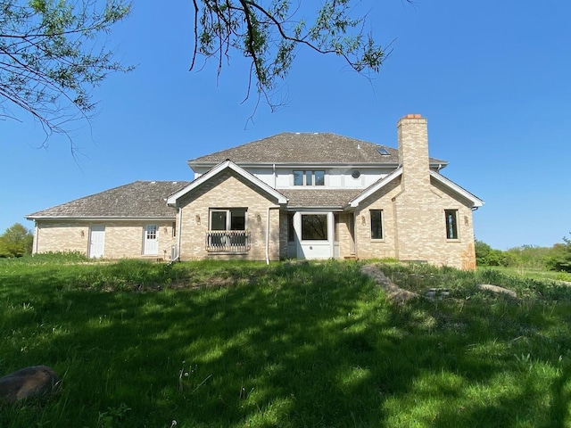 back of property featuring a chimney, brick siding, and a lawn