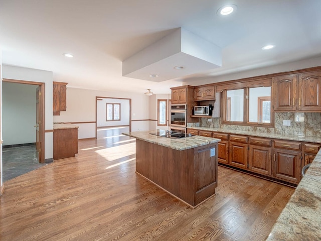 kitchen featuring appliances with stainless steel finishes, a kitchen island, tasteful backsplash, light stone countertops, and light wood-style flooring