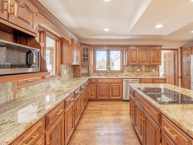 kitchen featuring appliances with stainless steel finishes, a sink, recessed lighting, light stone counters, and brown cabinetry