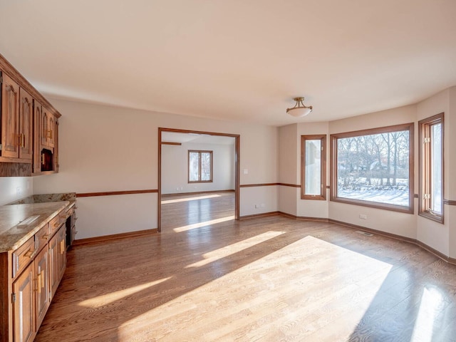 kitchen featuring light wood-type flooring, brown cabinets, baseboards, and light stone countertops