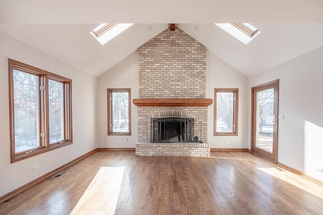 unfurnished living room featuring a skylight, light wood-style floors, a fireplace, baseboards, and high vaulted ceiling