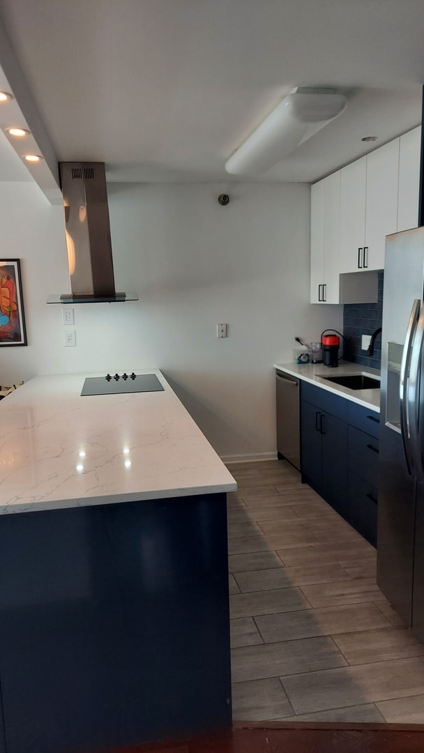 345 N La Salle Dr Unit 3305, Chicago, IL 60654 - kitchen featuring wall chimney range hood, stainless steel appliances, a sink, wood finish floors, and white cabinetry