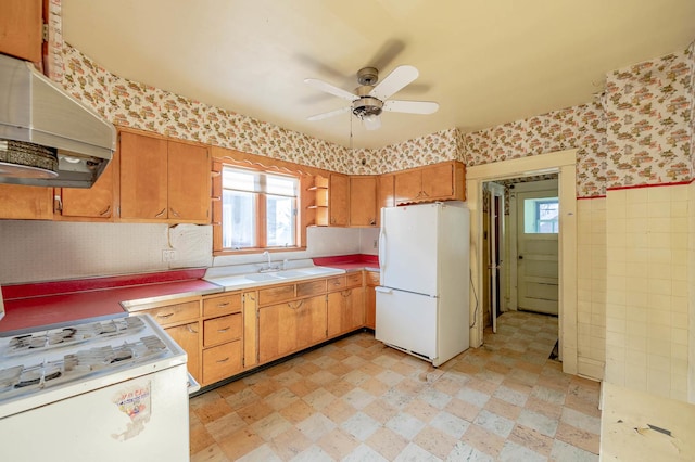 kitchen with white appliances, under cabinet range hood, wallpapered walls, ceiling fan, and plenty of natural light